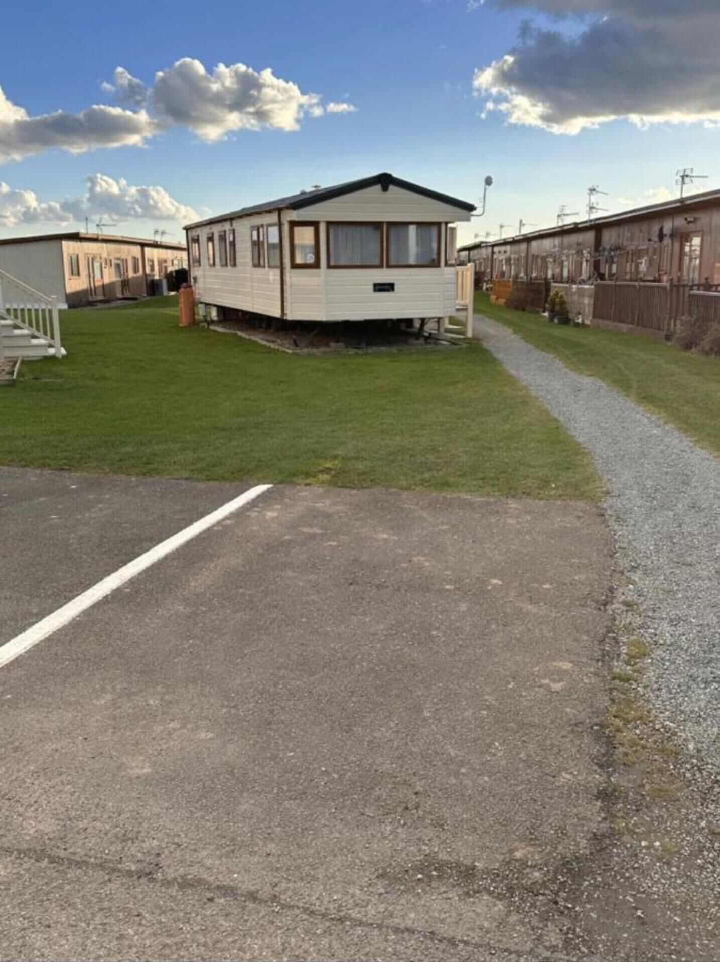 Un terrain de camping pour caravanes comprenant une seule caravane, un espace de stationnement dallé et un chemin bordé de pelouse.