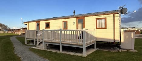 A single-story mobile home with a front porch, a satellite dish, and a gravel driveway.