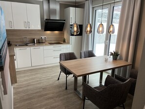 Une cuisine moderne avec des armoires blanches, un four encastré et un coin repas comprenant une table et des chaises en bois.