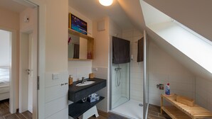 A modern bathroom with a shower, a vanity with a mirror, and a wooden bench.