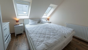 A bedroom with a large bed, two bedside tables, a dresser, and a skylight.