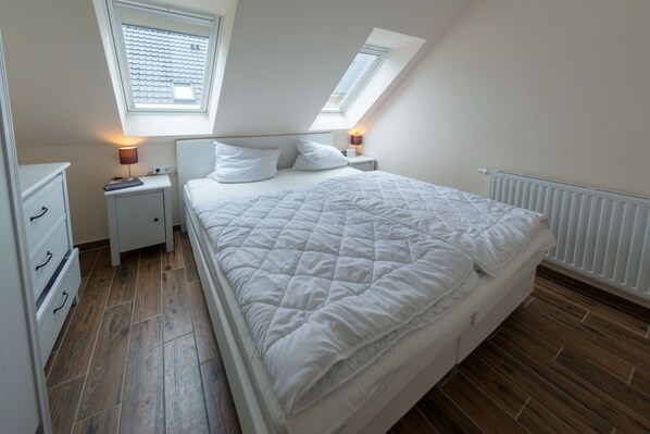 Une chambre à coucher avec un grand lit, deux tables de chevet, une commode et une lucarne.