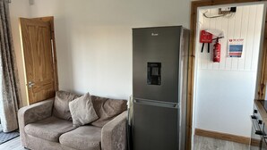 Ett kompakt bostadsutrymme med en soffa, ett kylskåp i rostfritt stål, en trädörr och en brandsläckare som är monterad på väggen.