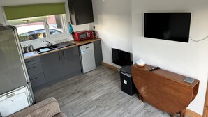 Ett kompakt kök med en inbyggd mikrovågsugn, ett litet kylskåp och en diskho. Det finns ett träbord och en tv som är monterad på väggen.