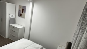 Ett hotellrum med en säng, en garderob, ett litet skrivbord och ett nattduksbord.