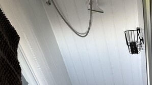 En duschplats med ett duschmunstycke som kan hållas i handen, en kontrollpanel och en handdukshängare.