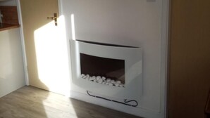 A room with a flat-screen TV mounted above a white fireplace with a stone surround. - Chalet Retreat in Mablethorpe (Mablethorpe)