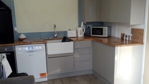 A compact kitchen with a dishwasher, microwave, and toaster. There is a wooden countertop and a grey sofa in the living area. - Chalet Retreat in Mablethorpe (Mablethorpe)