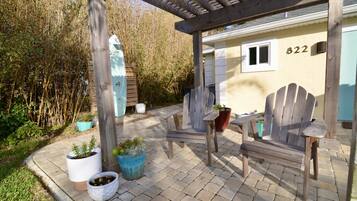 Een houten pergola met een bankje en potplanten, een huis met nummer 822, en een bamboomschutting op de achtergrond.