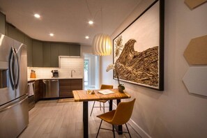 Una cocina moderna con área de comedor, que presenta una obra de arte grande en la pared, una mesa de madera y una silla amarilla.