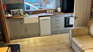 A compact kitchen with a microwave, dishwasher, and a small oven. There is a window with a view of a building outside. - Lovely 1-bed Chalet in Mablethorpe (Mablethorpe)