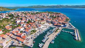 Vista aerea di una cittadina costiera con un porto turistico, edifici e una chiesa imponente.