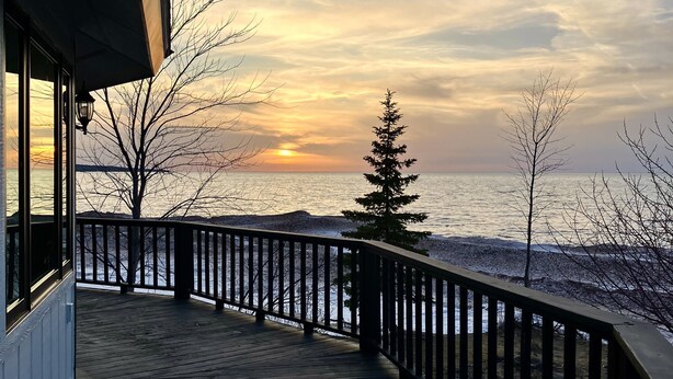 A wooden deck with a railing overlooking a body of water during sunset. - Your Superior Vacation Destination  (Ontonagon)