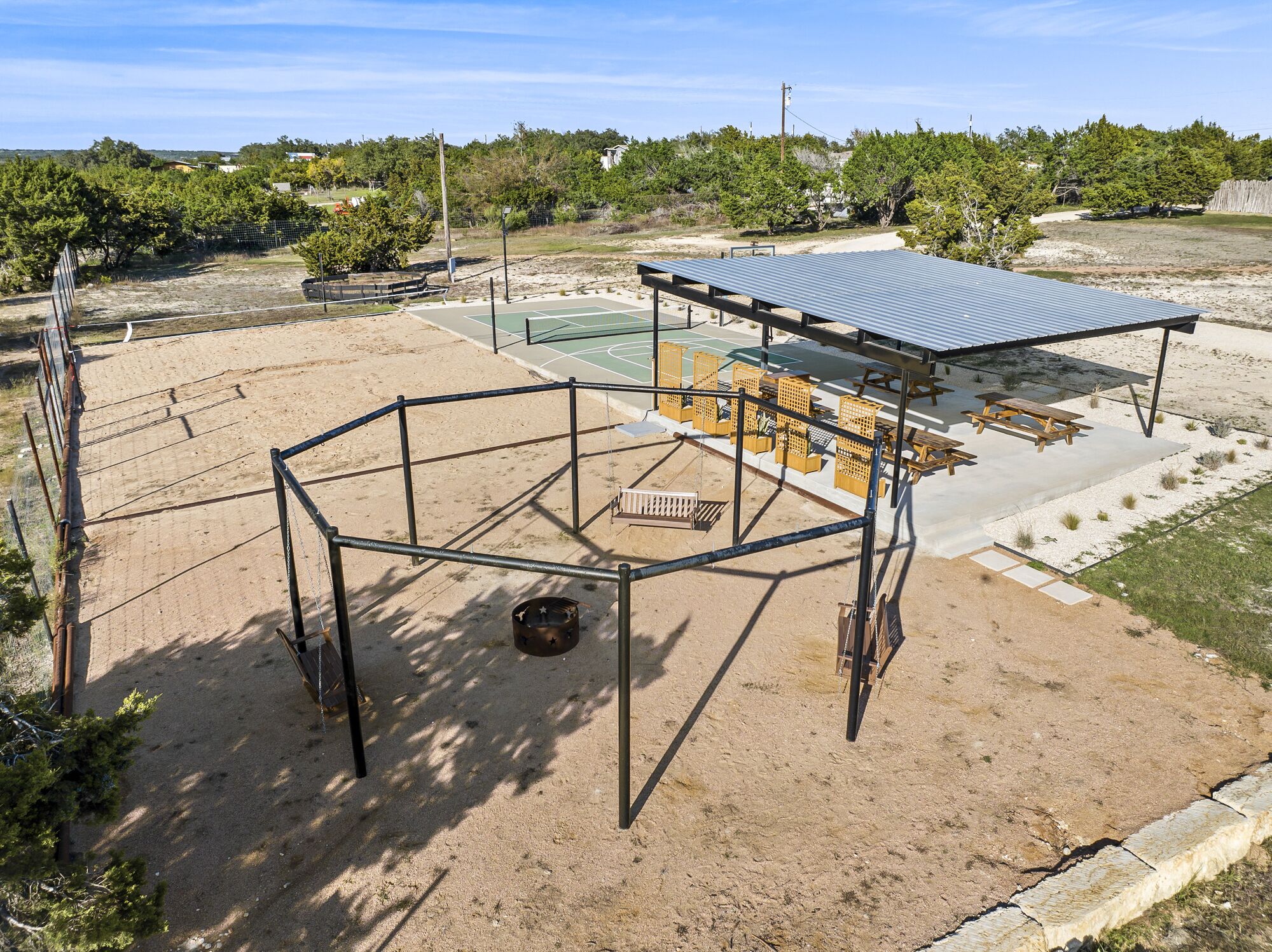 A metal structure with a roof, surrounded by sand, with a basketball court and picnic tables nearby.