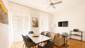 A modern living room with a dining area, a sofa, a TV, and a bookshelf. - Lumina Hidden Terrace - Charming Family Apartment in the Heart of Perugia (Perugia)