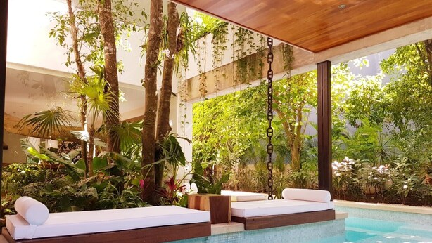 Una piscina interior con dos sillas reclinables blancas y una terraza de madera.