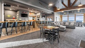 Un grand espace bar avec un comptoir et des sièges, un coin salon confortable avec un canapé et des fauteuils, et de grandes fenêtres offrant une vue panoramique.