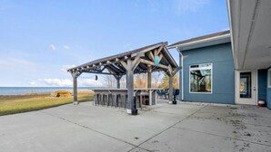 Un espace extérieur abrité avec des tables et des chaises, un bâtiment à la façade bleue et une vue sur la plage.