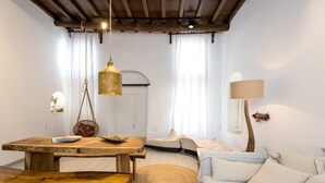 A cozy living room with a wooden table, bench, and sofa, featuring a hanging light fixture and a lamp. - Villa Loom Mykonos Town (Mykonos)