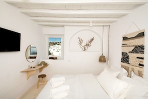 Une chambre à coucher minimaliste, avec un lit, une table de chevet, un miroir et une fenêtre donnant sur des immeubles.