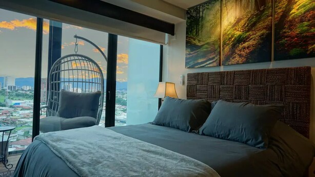 A modern hotel room with a large bed, a hanging chair, and a city view.