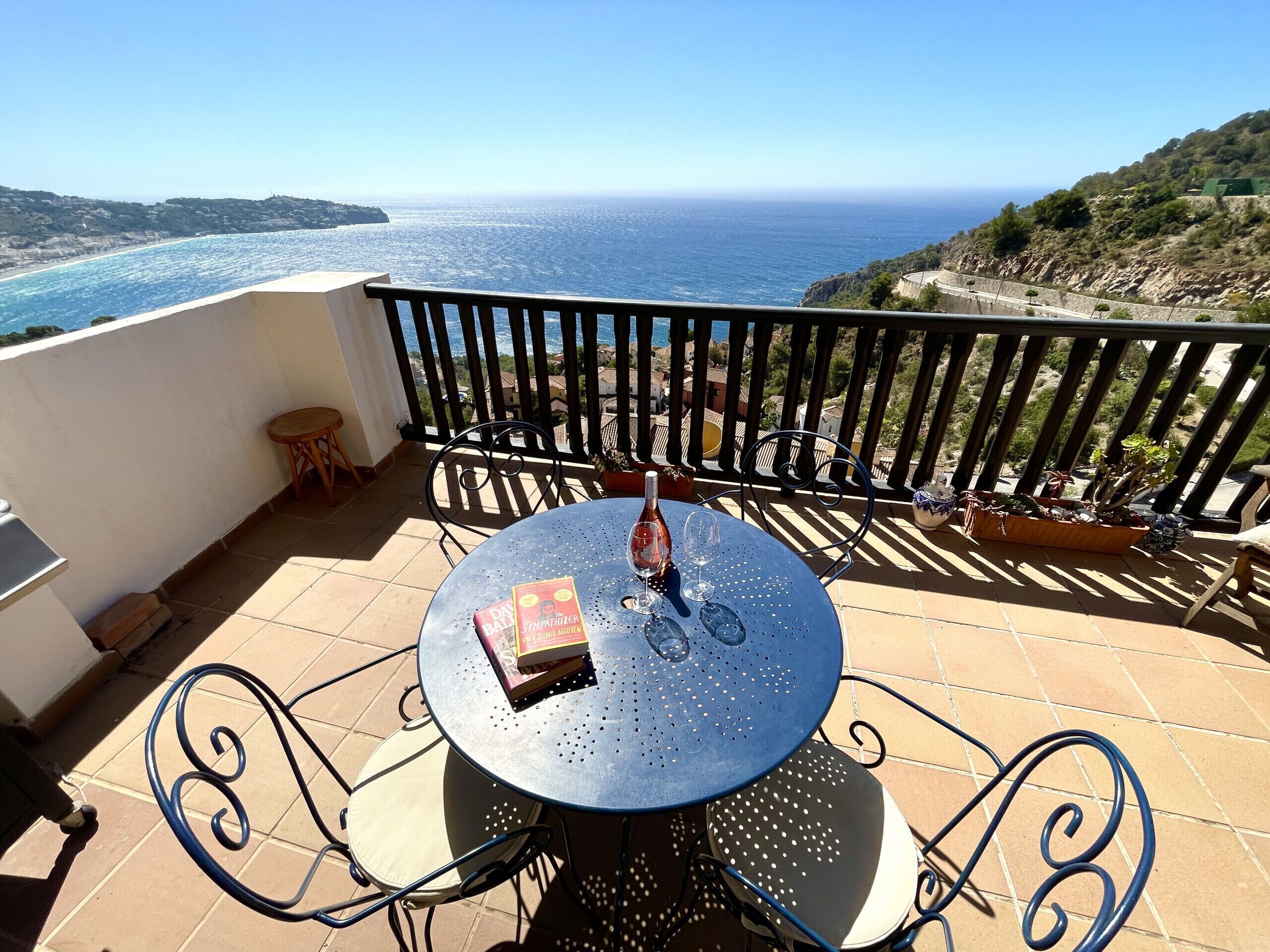 Une table ronde entourée de chaises, sur un balcon donnant sur la mer.