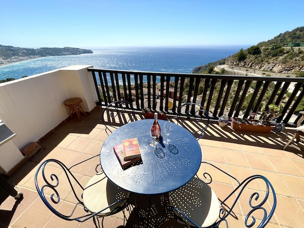 A round table with chairs on a balcony overlooking the sea.
