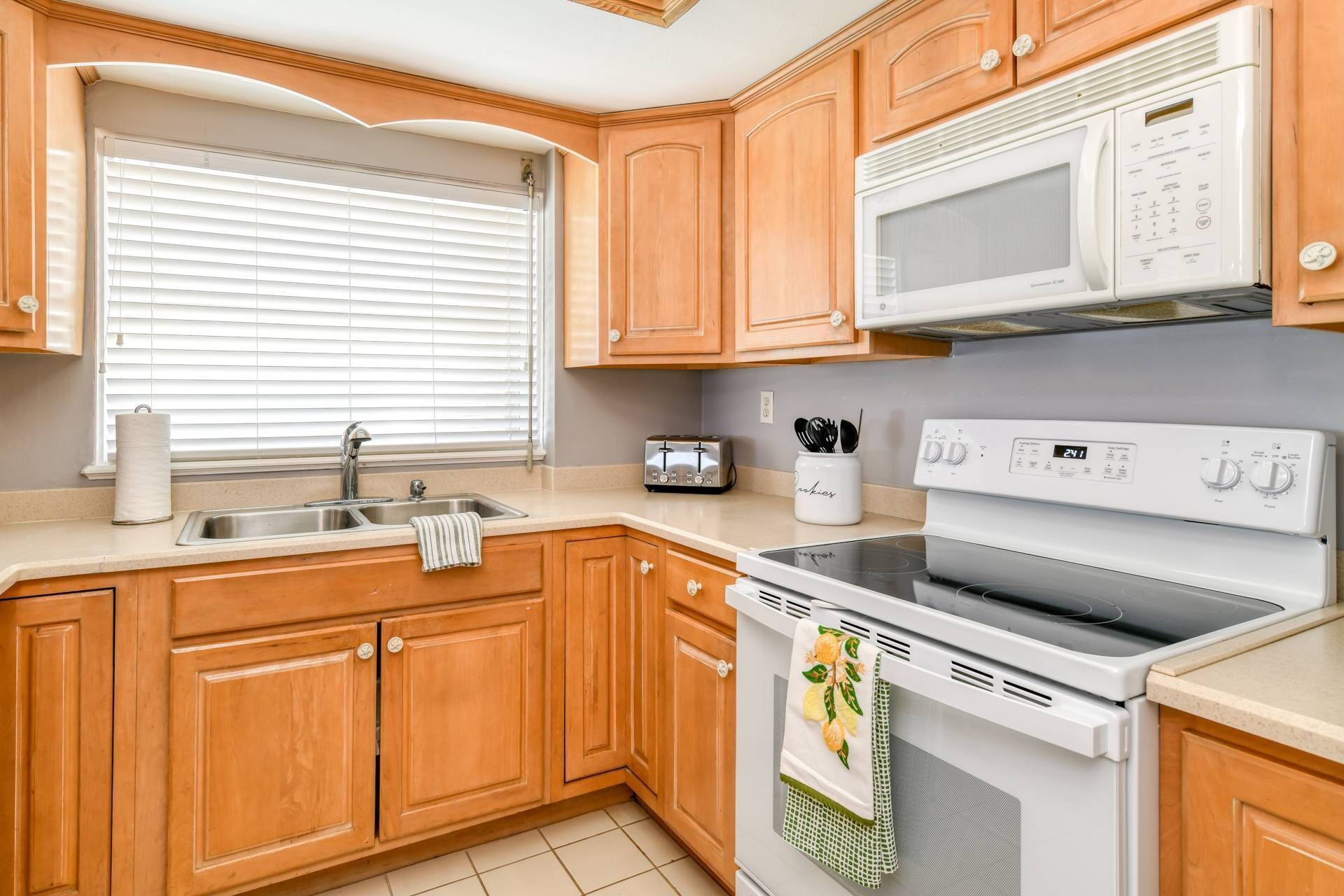 A kitchen with wooden cabinets, a stainless steel sink, a microwave, a toaster, and a stove.