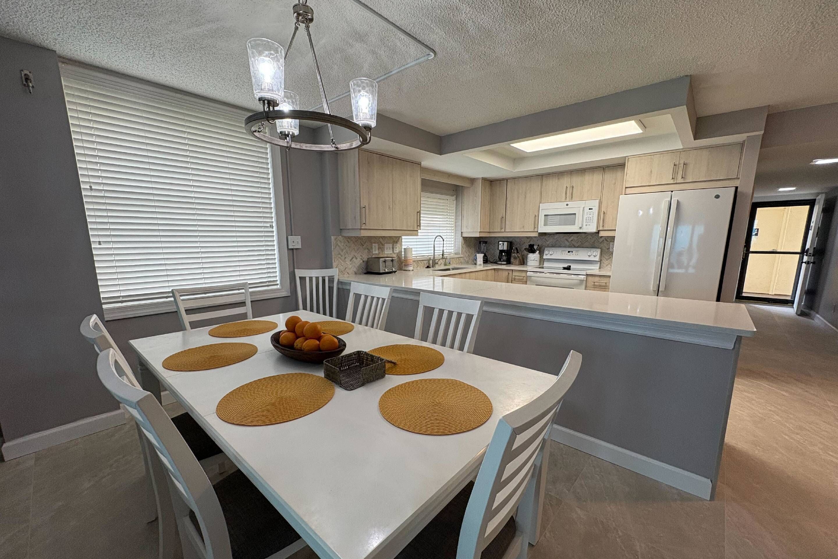 A modern kitchen with a central island, white cabinetry, and a dining area with a white table and chairs.