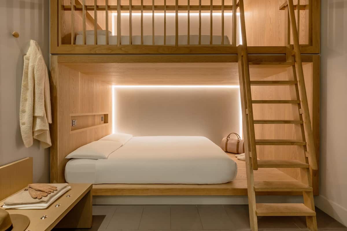 A bunk bed room with a wooden ladder, a bedside table, and a wall-mounted shelf.