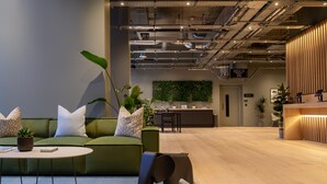 A modern office space with a green sofa, a small elephant sculpture, a reception desk, and a green wall with plants. - Zedwell Greenwich (London)