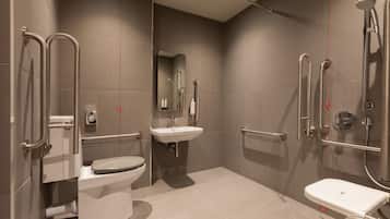 A modern bathroom with a toilet, sink, and shower area, equipped with grab bars and a handrail.