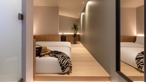 A modern hotel room with a minimalist design, featuring a large mirror, a sofa with a patterned throw, and a small potted plant. - Zedwell Greenwich (London)