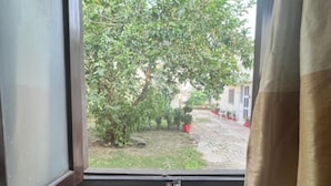 Une fenêtre donnant sur un jardin, avec un bâtiment visible au loin.
