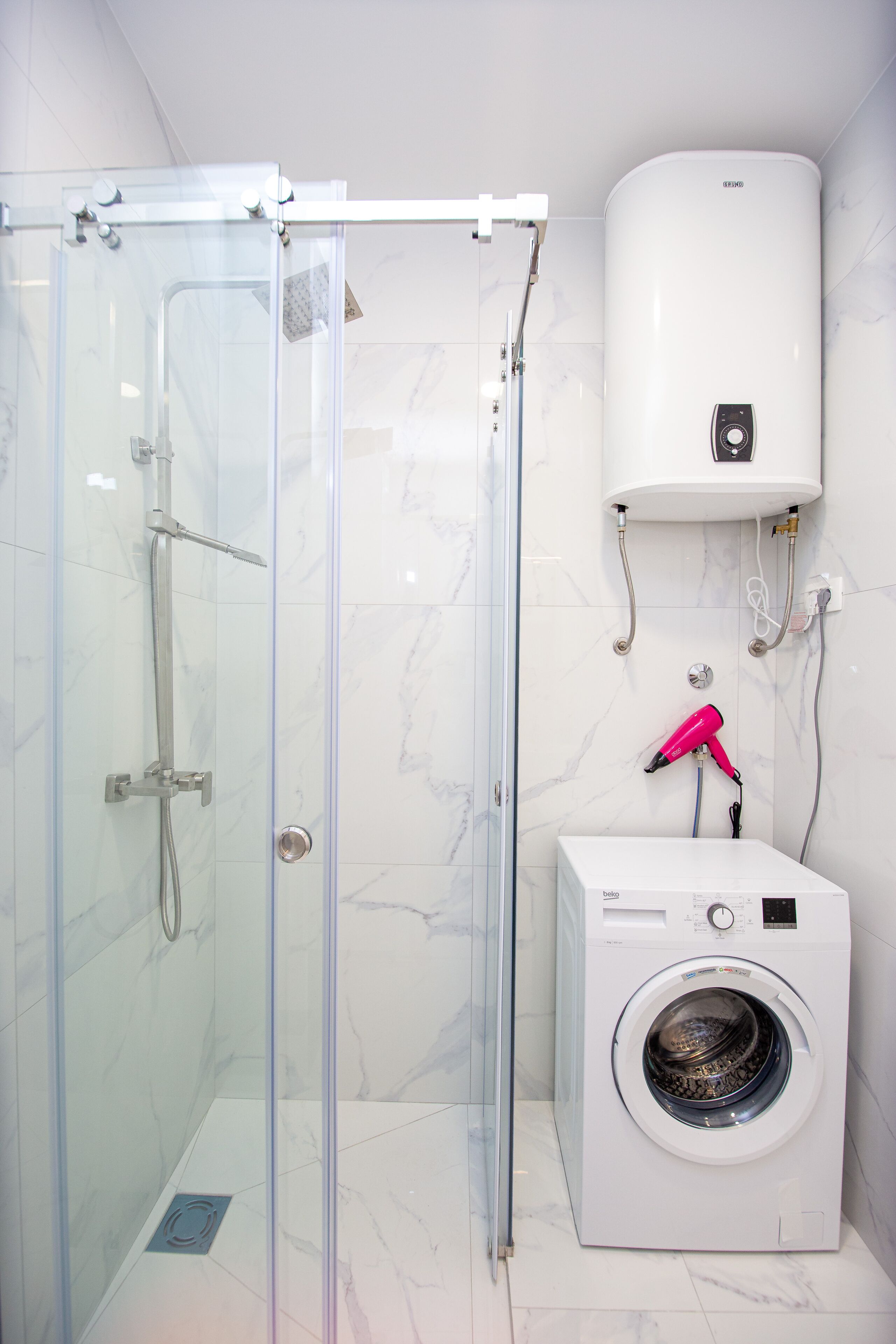 Un baño con ducha acristalada, calentador de pared y lavadora de carga frontal.