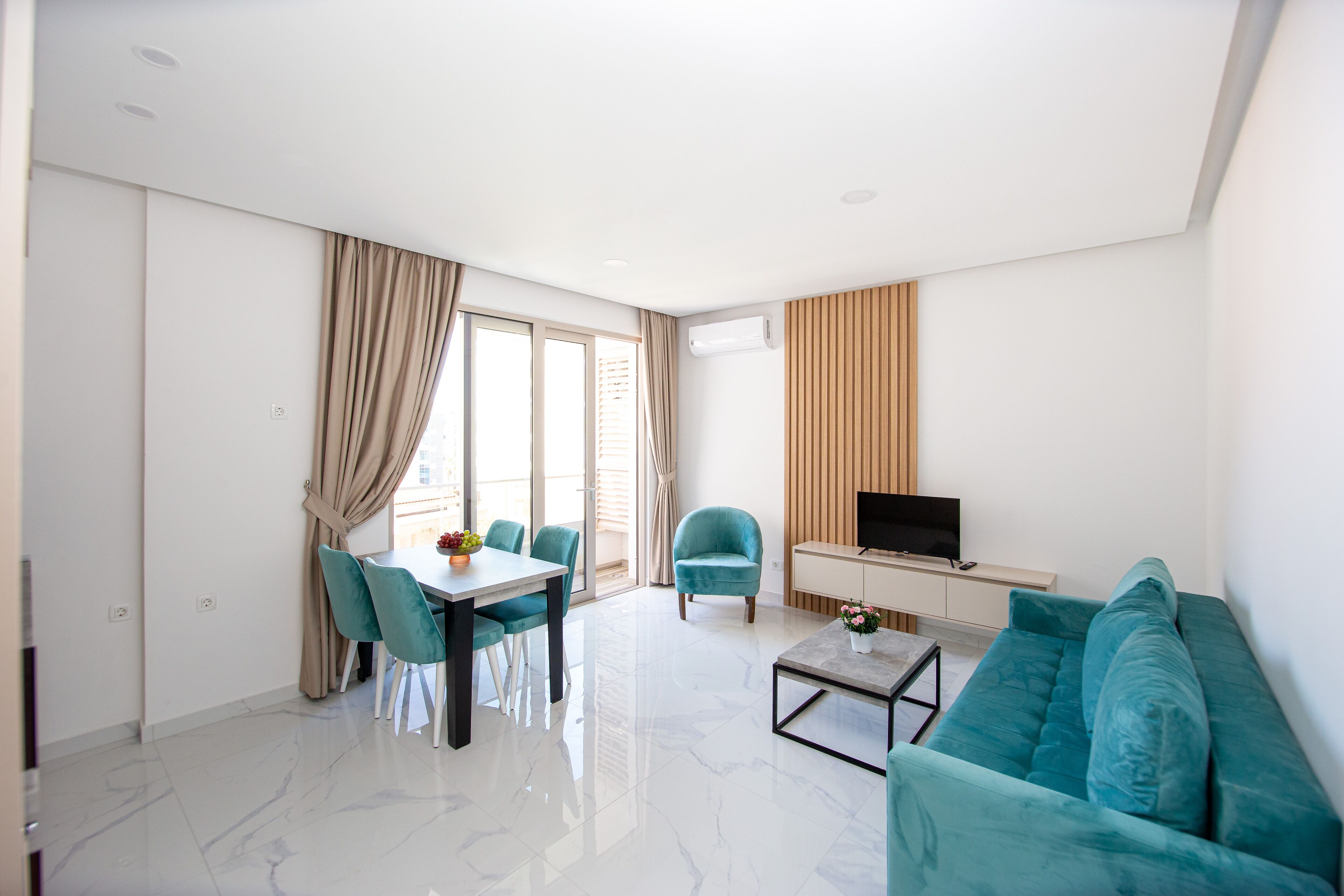 A modern living room with a sofa, a TV, a dining table with chairs, and a large window with curtains.