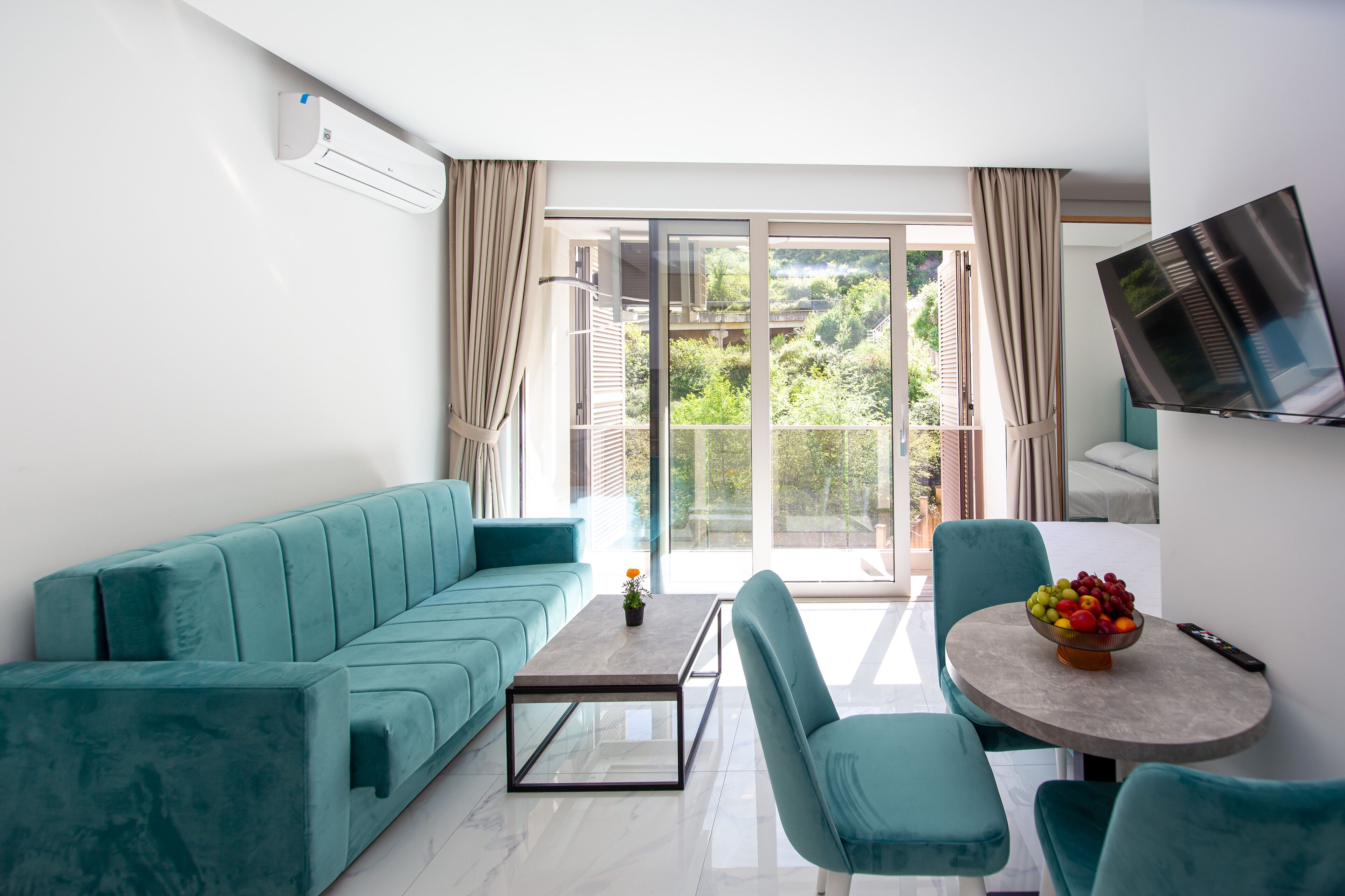 Un salon moderne avec un canapé de couleur turquoise, une table basse et un coin repas comprenant des chaises et un panier de fruits.