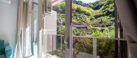 A balcony with a glass door, a view of a bridge, and a lush green hillside.