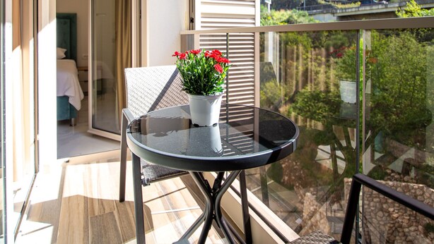 A balcony with a table and chairs, a potted plant, and a view of a lush green landscape. - IN Property Apartments (Becici)