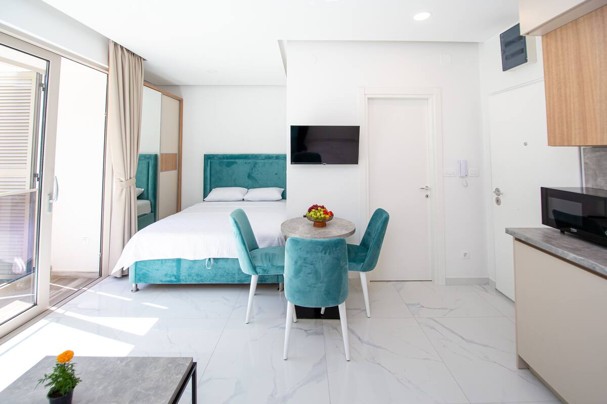 A modern bedroom with a bed, a TV, and a dining area with chairs and a table.