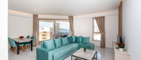 A modern living room with a teal sofa, a dining table with chairs, a coffee table, and a TV on a stand.