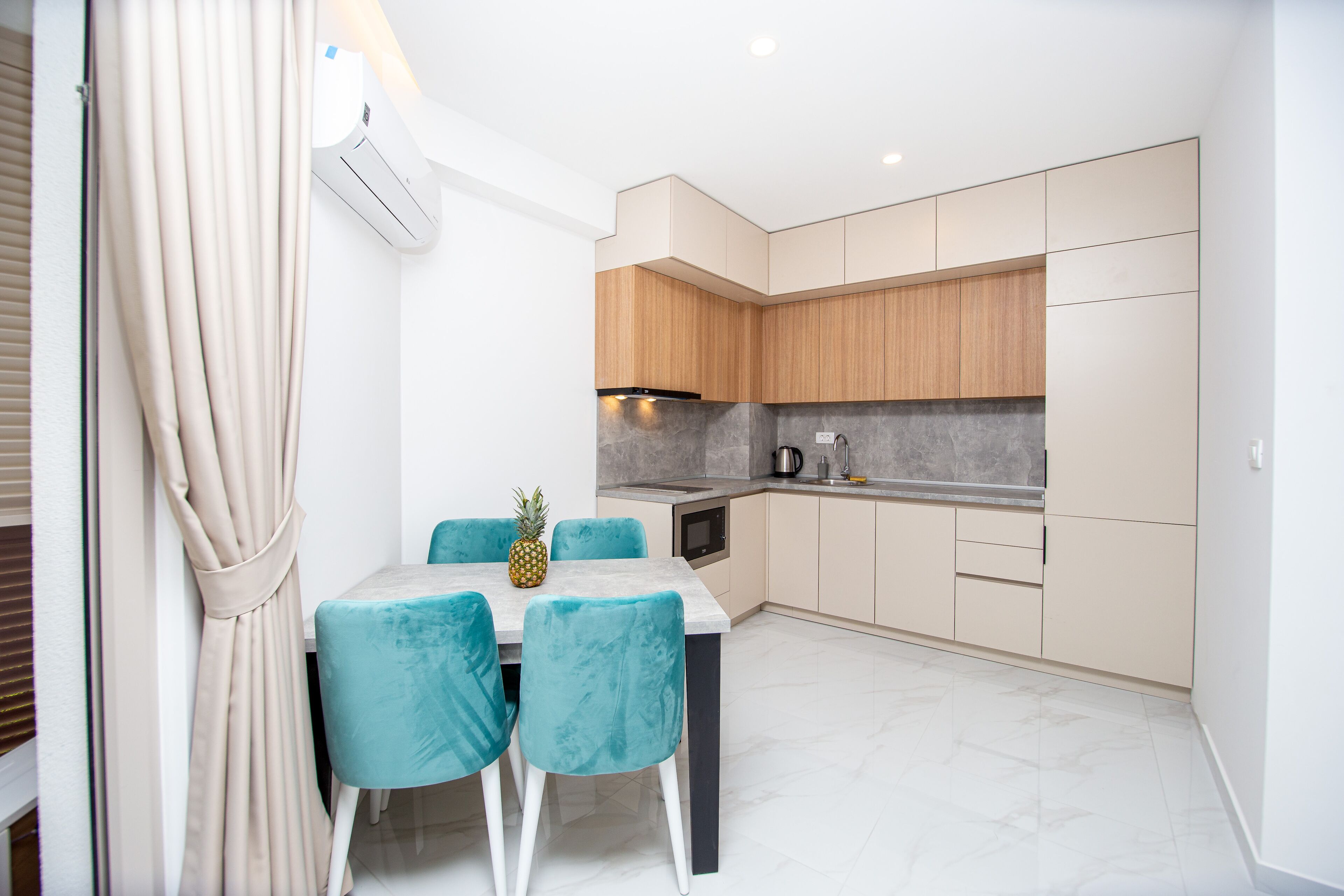 A modern kitchen with light wood cabinets, a granite countertop, and a dining area with a table and chairs.