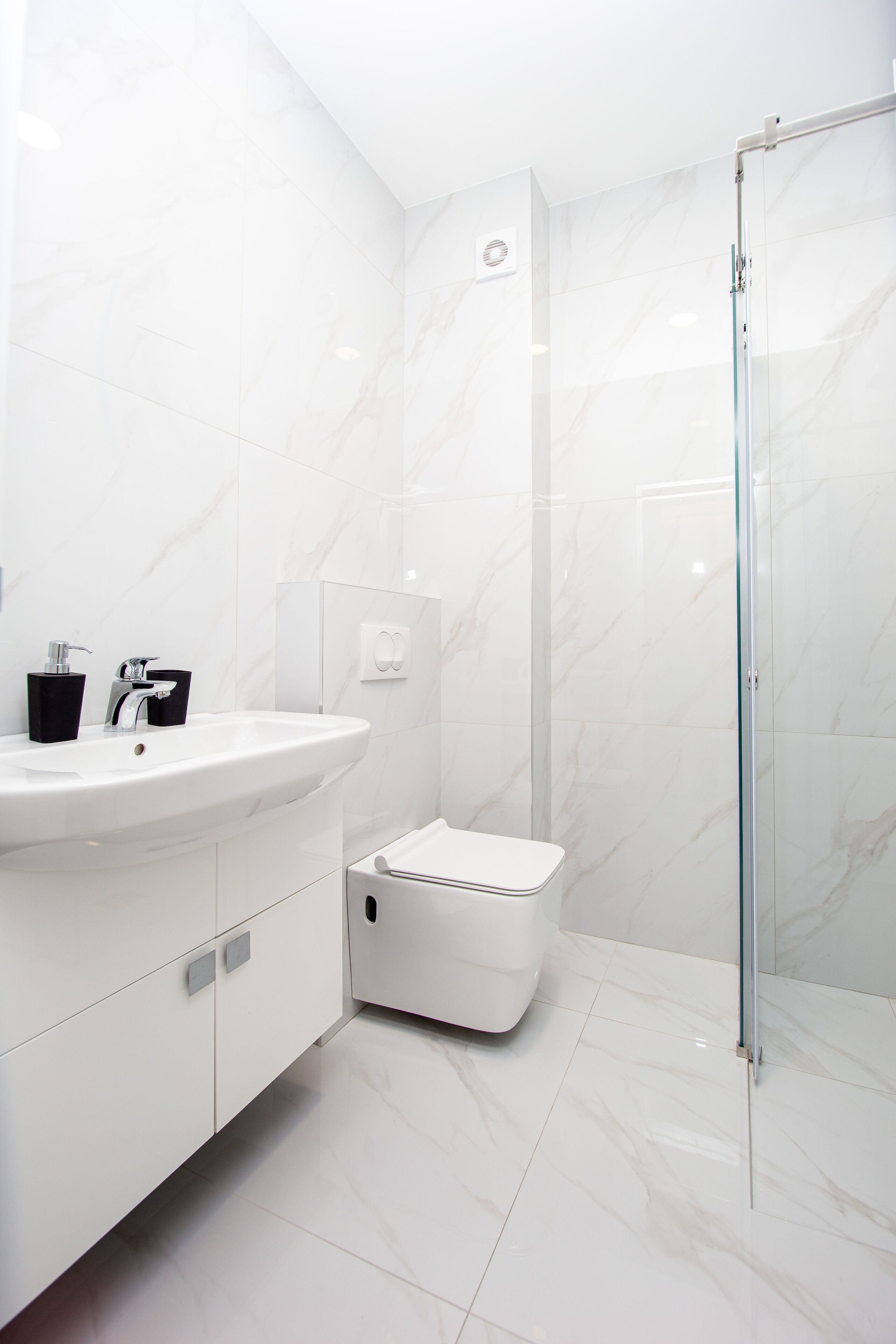 A modern bathroom with a white sink, black soap dispenser, and a glass shower enclosure.