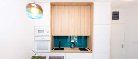A modern kitchen with white cabinets, a wooden countertop, a sink, and a coffee maker. There is a dining table with chairs and a potted plant.
