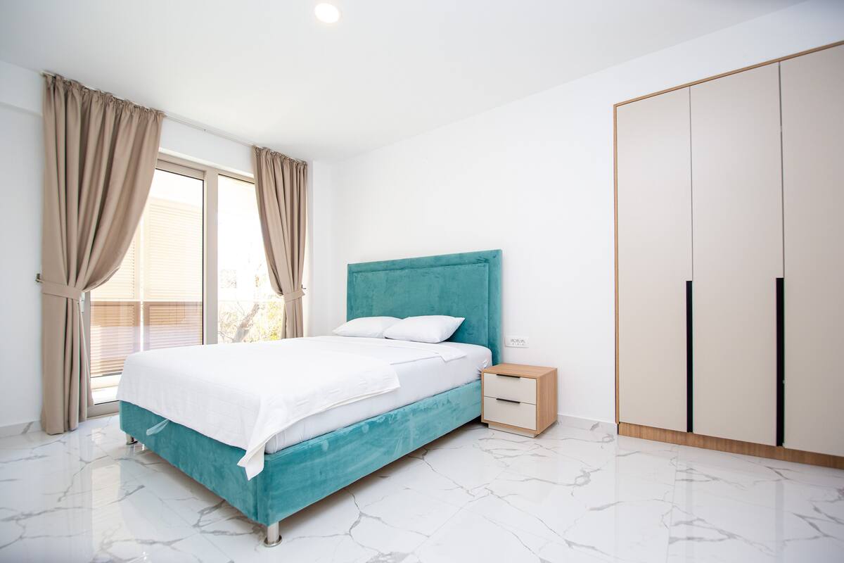 A bedroom with a bed, a nightstand, a wardrobe, and a window with curtains.