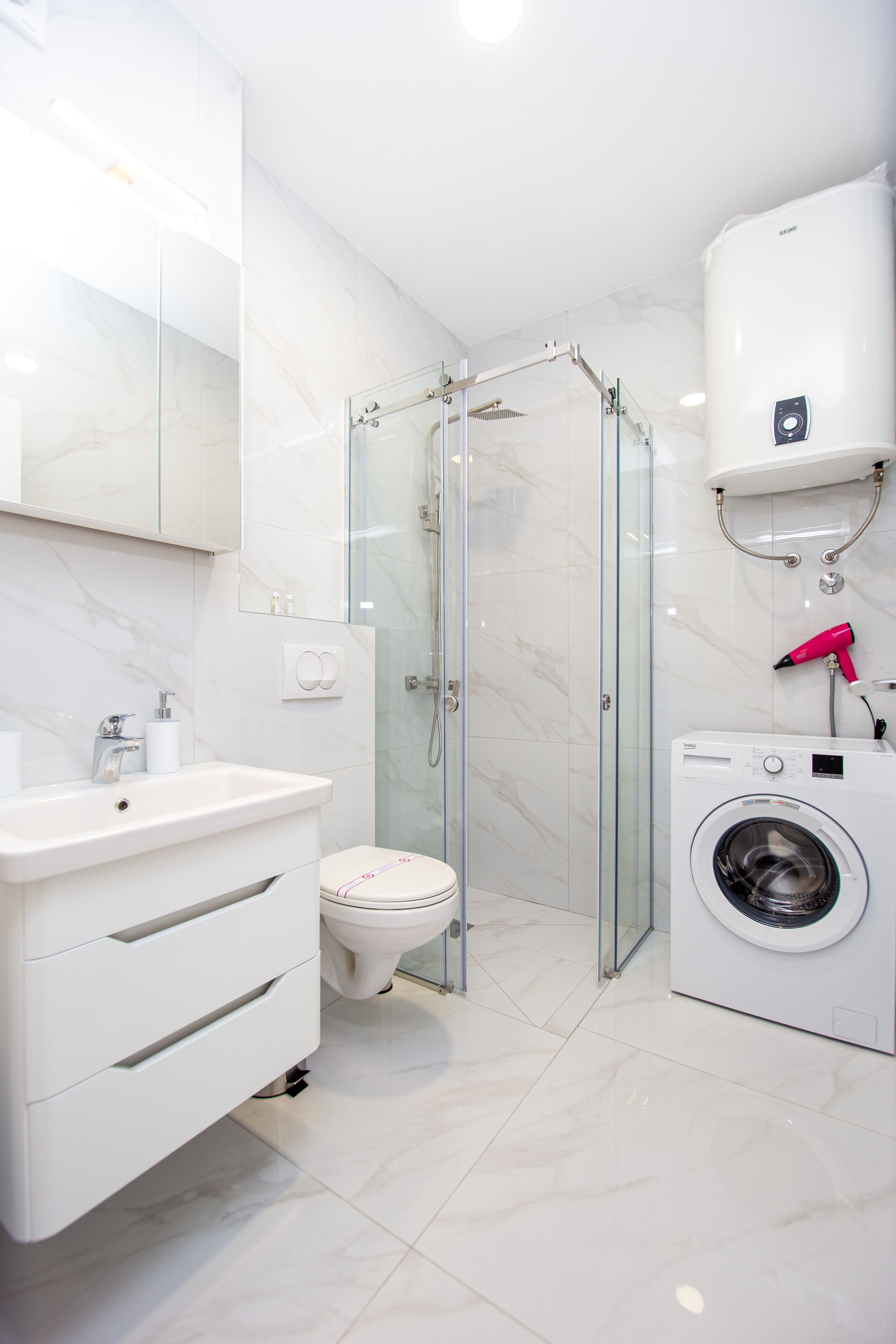 A modern bathroom with a glass-enclosed shower, a white sink, a toilet, and a washing machine.