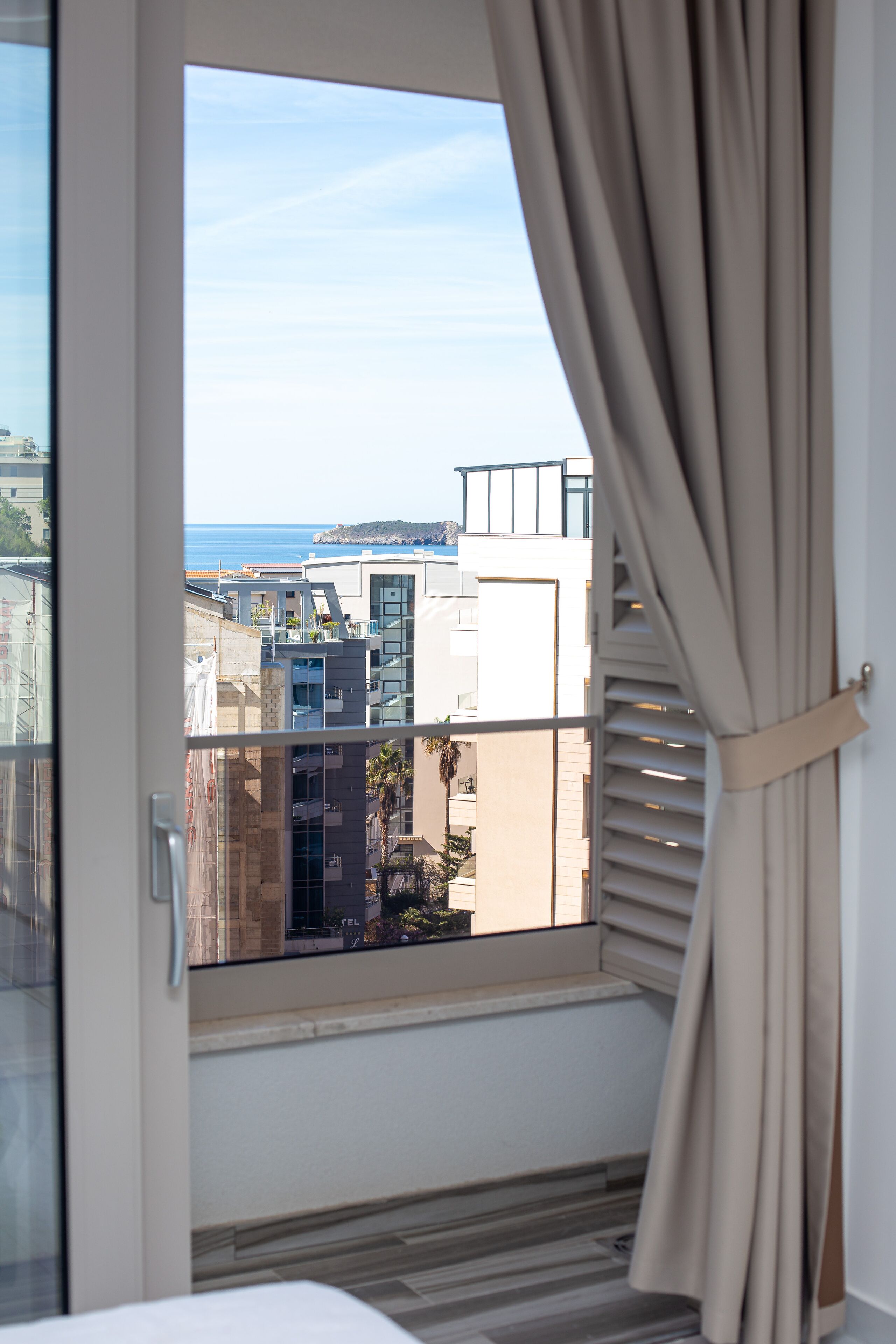 A room with a large window, a view of the sea, and a balcony with a railing.