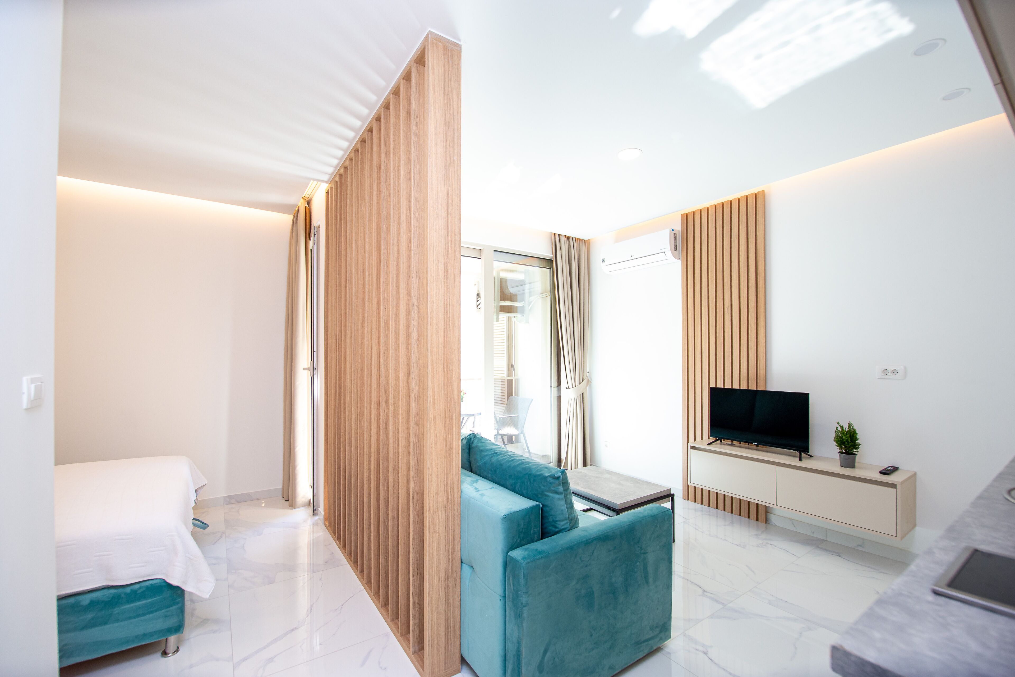A modern hotel room with a bed, a sofa, a TV, and a small table.