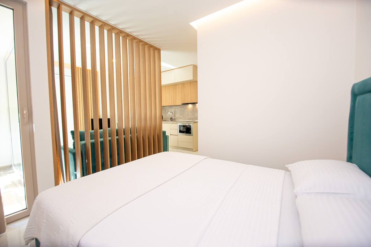 A hotel room with a bed, a view of the kitchen, and a sliding door.