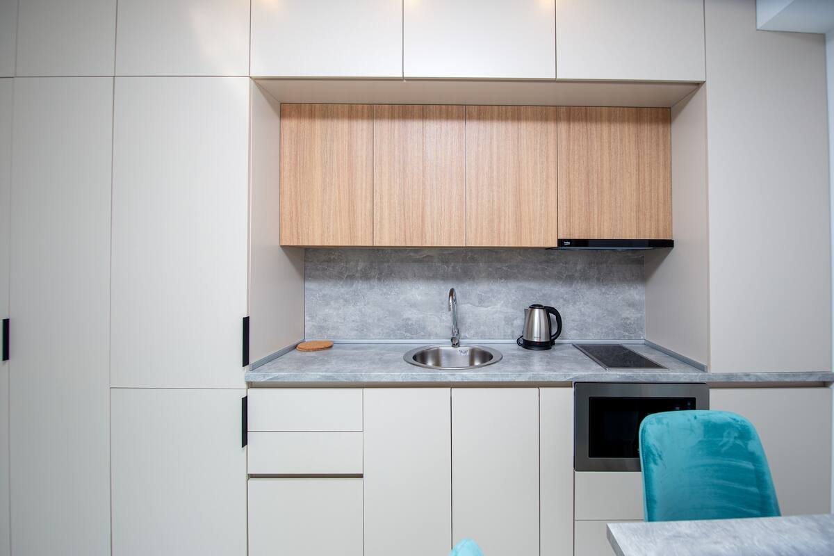 A modern kitchen with white cabinets, a stainless steel sink, a kettle, and a built-in oven.